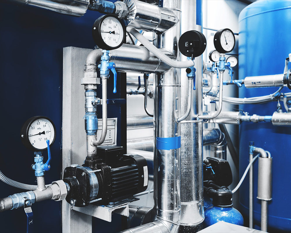 Stainless steel pipework with pressure gauges, blue hand valves and blue pressure vessels inside an industrial plant room