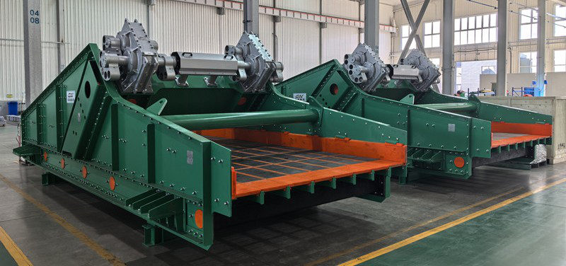 Two large green vibrating screening machines with orange screen decks standing in a manufacturing workshop